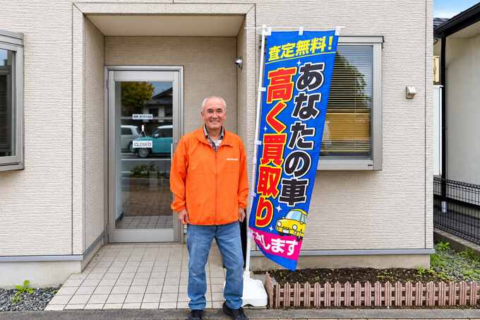 奥州車買取本舗の店舗入口で笑顔を見せる小野店長